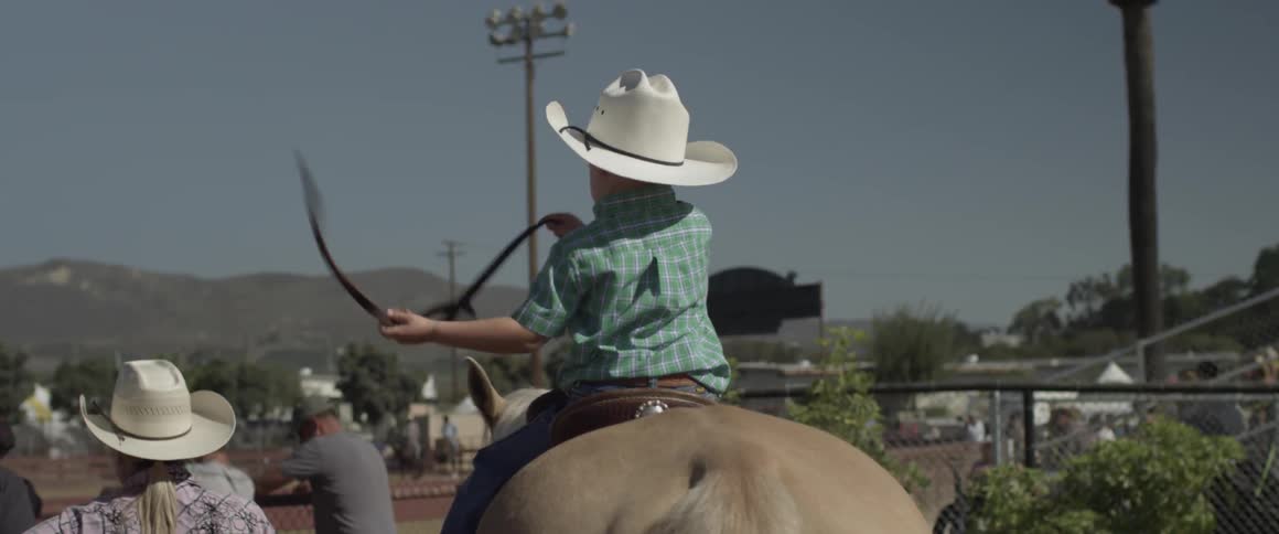Child sits on a horse waving a piece of rope