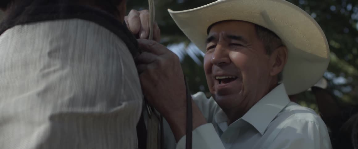A cowboy adjusts a vest a harness on another man