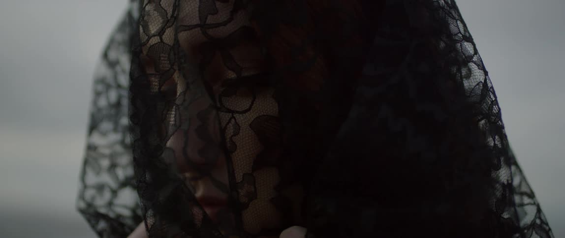 A woman wearing a black lace veil shifts her gaze and head downward