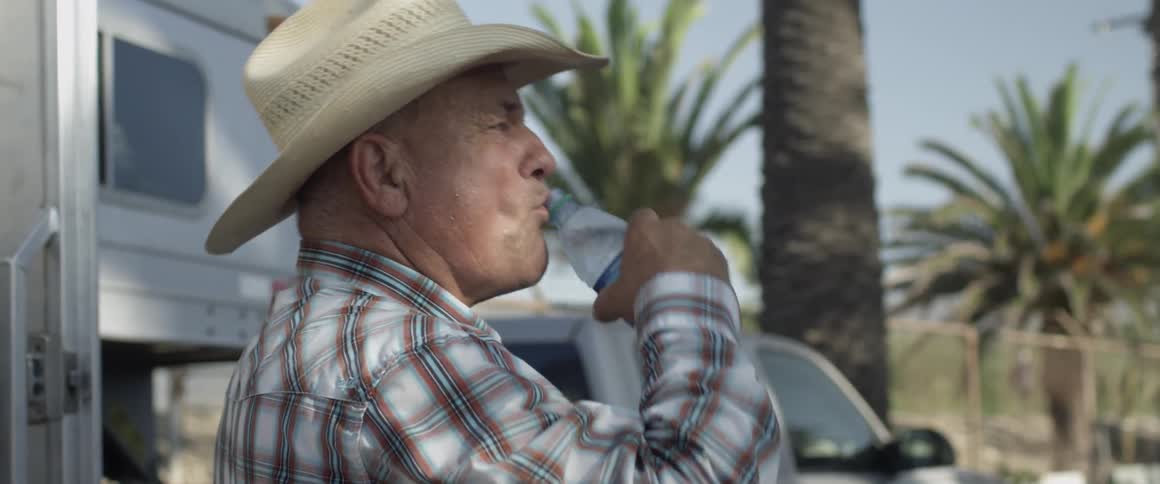 A man takes a drink near a trailer