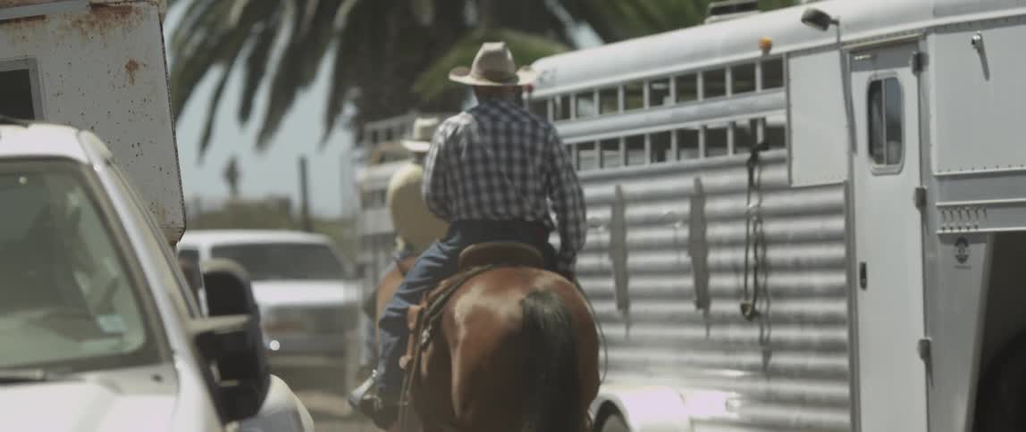 Two men riding horses between trailers