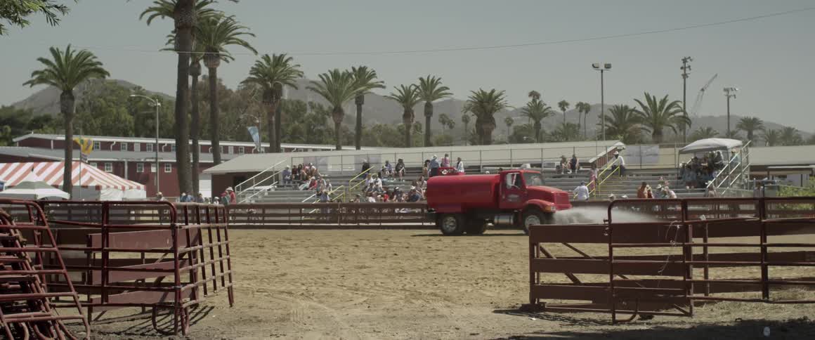 A red truck waters a sandy enclosed area
