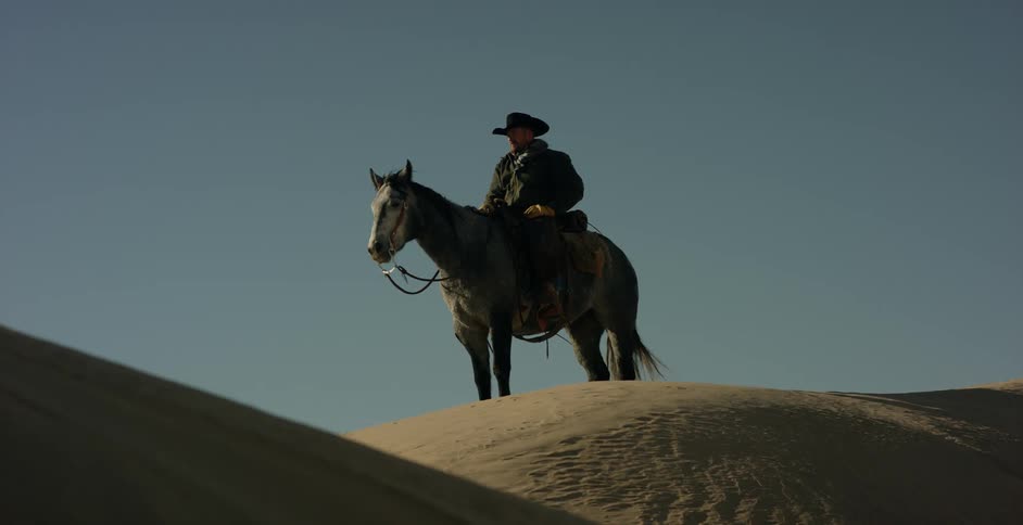 A man sitting on a horse on top of a sand dune