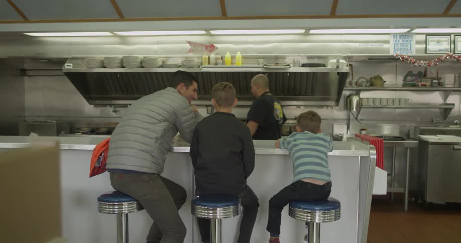 A man and two boys sit on stools in a diner