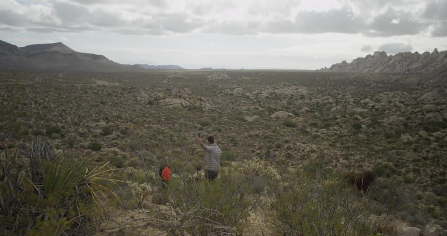 A man films his sons on a cell phone as they walk down a hill