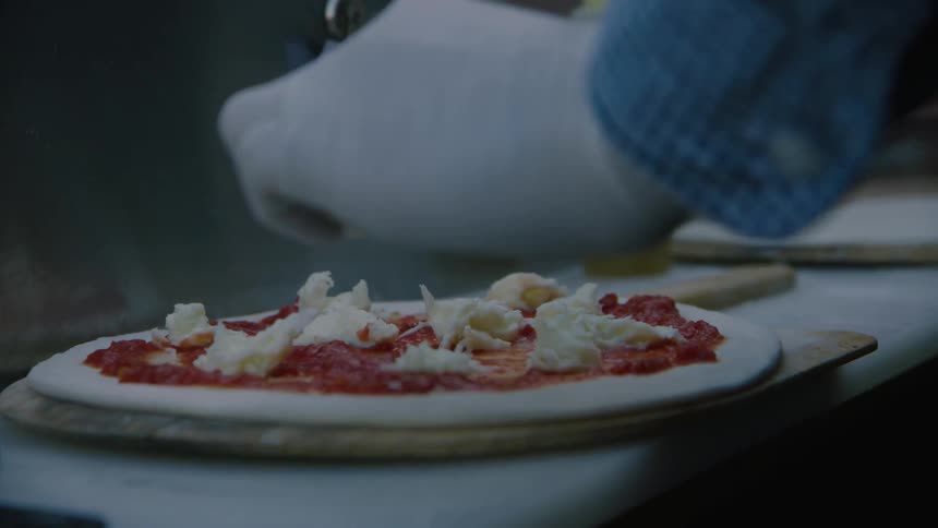 A restaurant worker puts cheese on a pizza