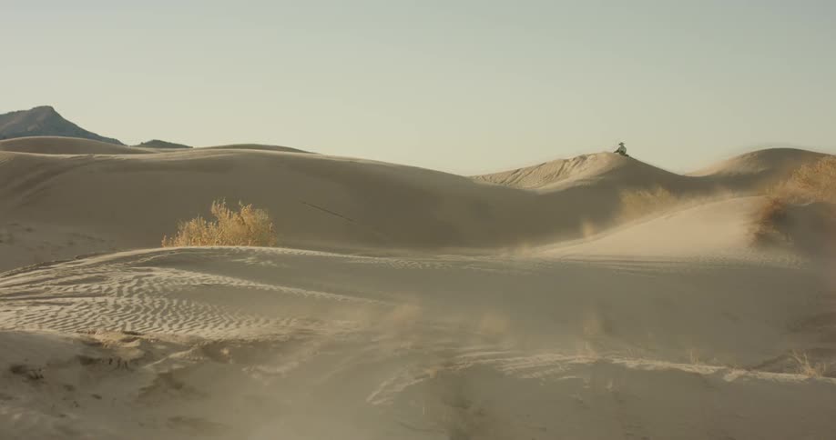 A person rides a horse over sand dunes and ridges