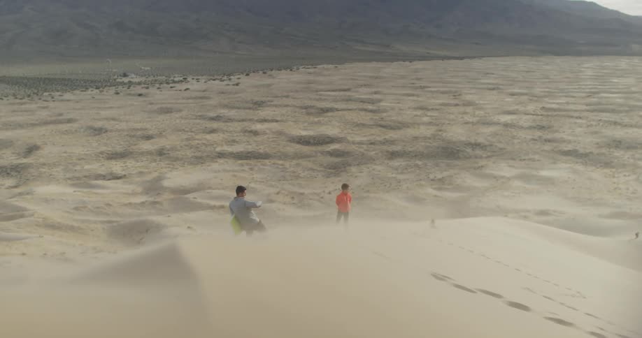 A man and boy stand on a sand dune on a windy day
