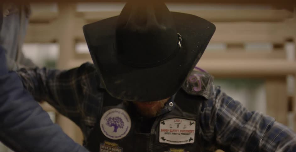 A rodeo rider eases himself down on an animal in the chute
