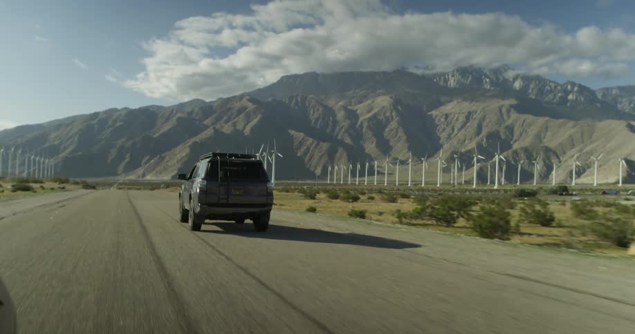 An suv drives down a road nearing windmills