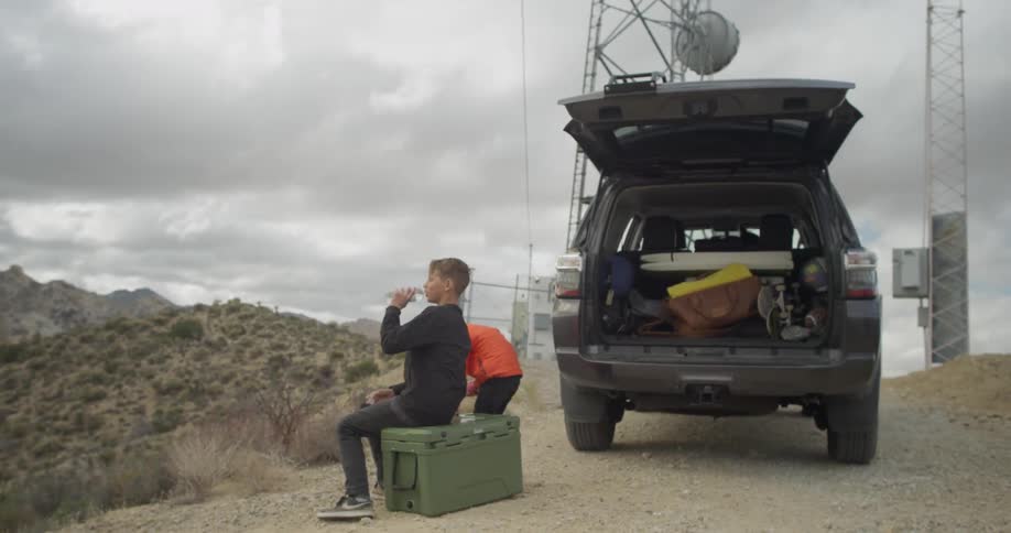 Two boys stand near a car parked in the desert