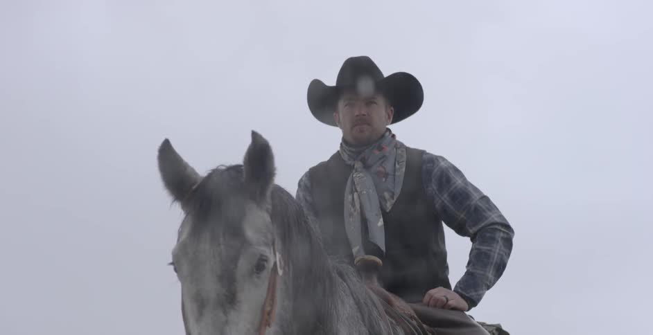A cowboy rides a horse while it snows