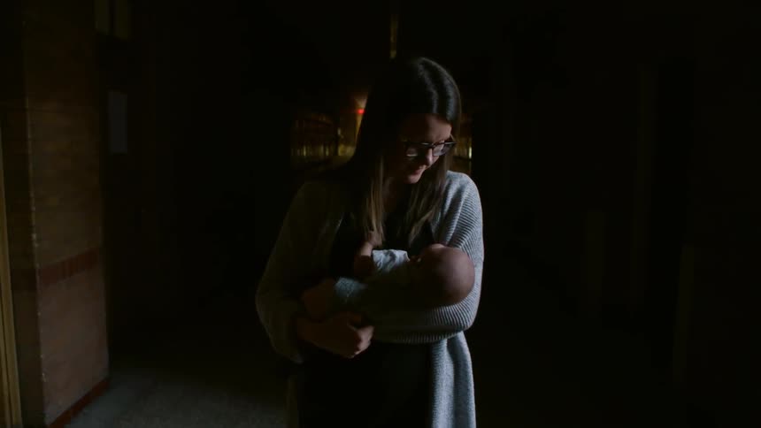 A woman holds an infant while walking down the hall