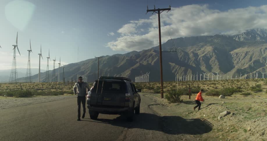 A child exits a truck and runs towards a field as a man catches up