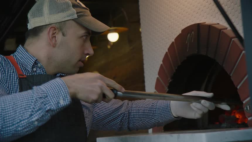 A man is tending the fire in a pizza oven