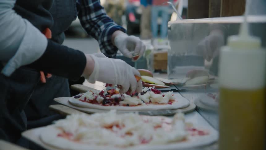 Restaurant workers sprinkle toppings on pizza