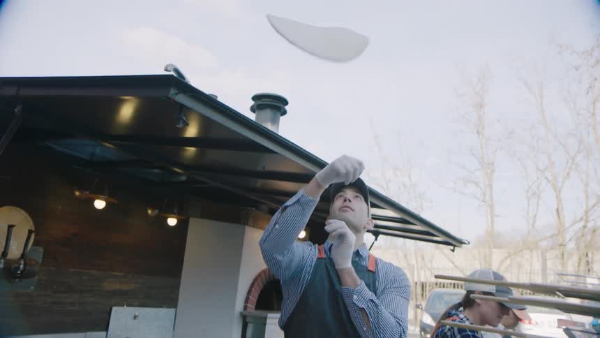 Man twirling and throwing pizza dough into the air outside