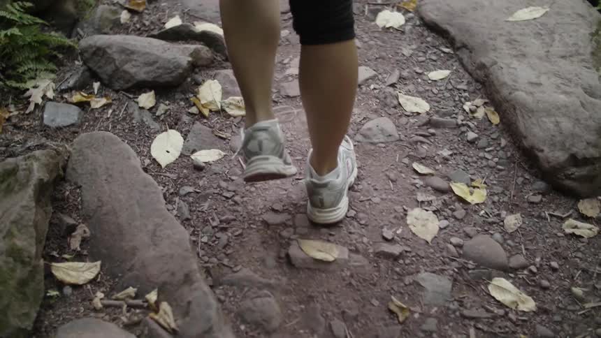 A woman walks over rocks on a forest path