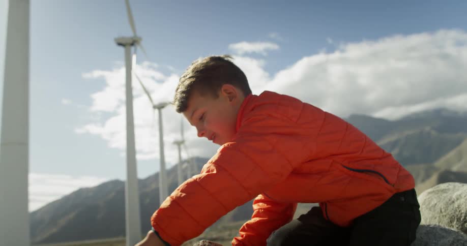 A boy playing in the sand with a rock near some big fans