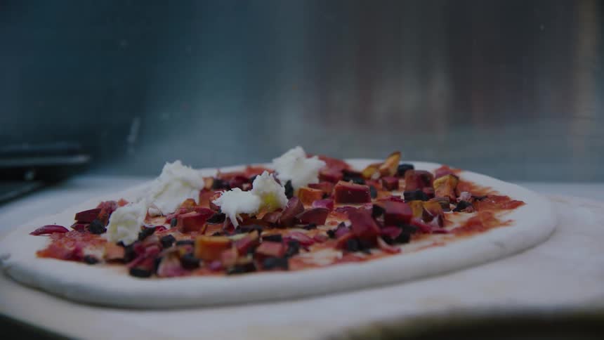 A person adds toppings to a pizza before baking