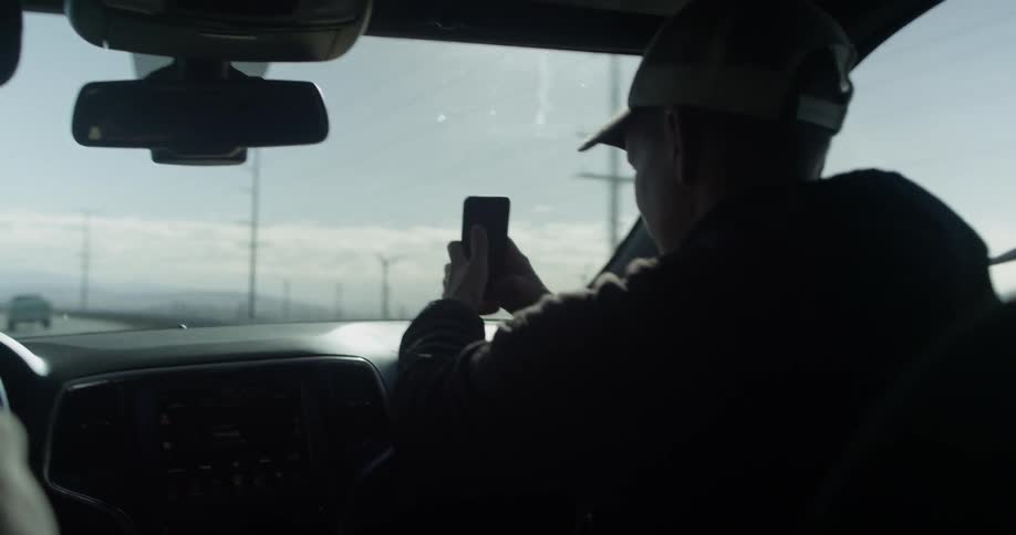 A boy is filming through a vehicle window using his cell phone as it travels