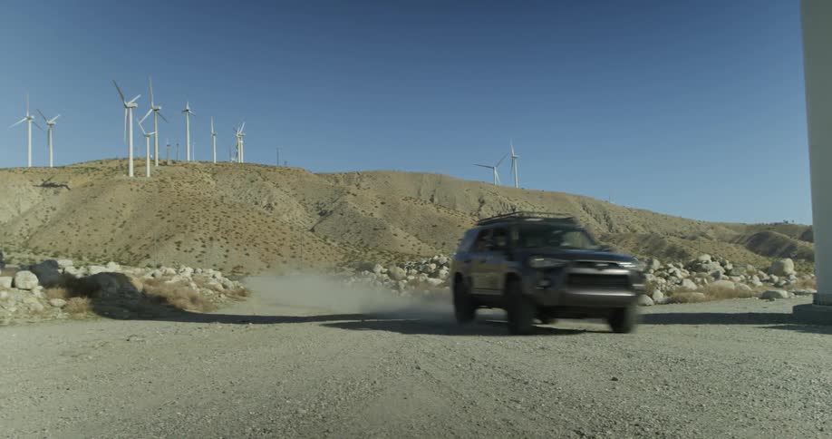 A black car speeds down a gravelly road