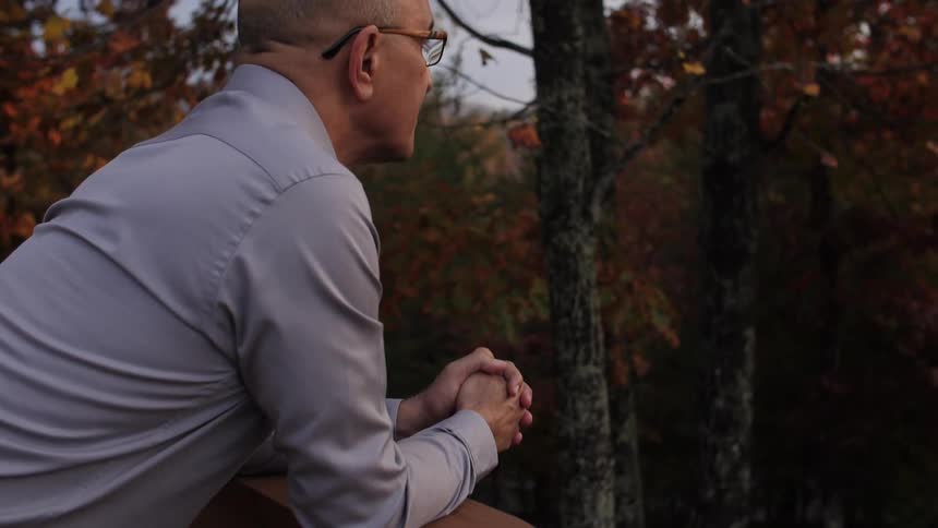 A man stands on a deck overlooking fall trees