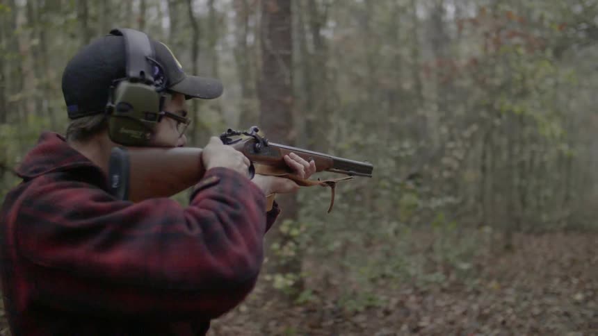 A man lifts is rifle, and fires into the woods