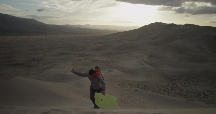 A man hikes up a sand dune with a boy on his back