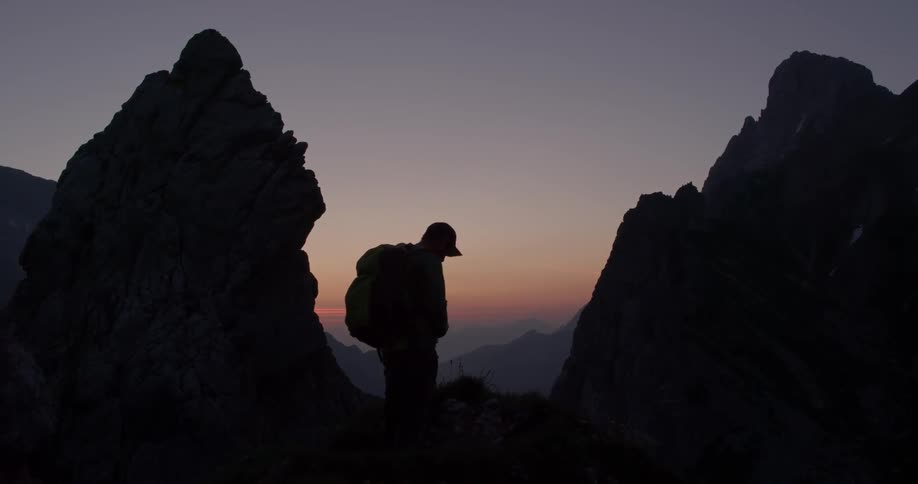 A man picks up a backpack and puts it on at sunrise