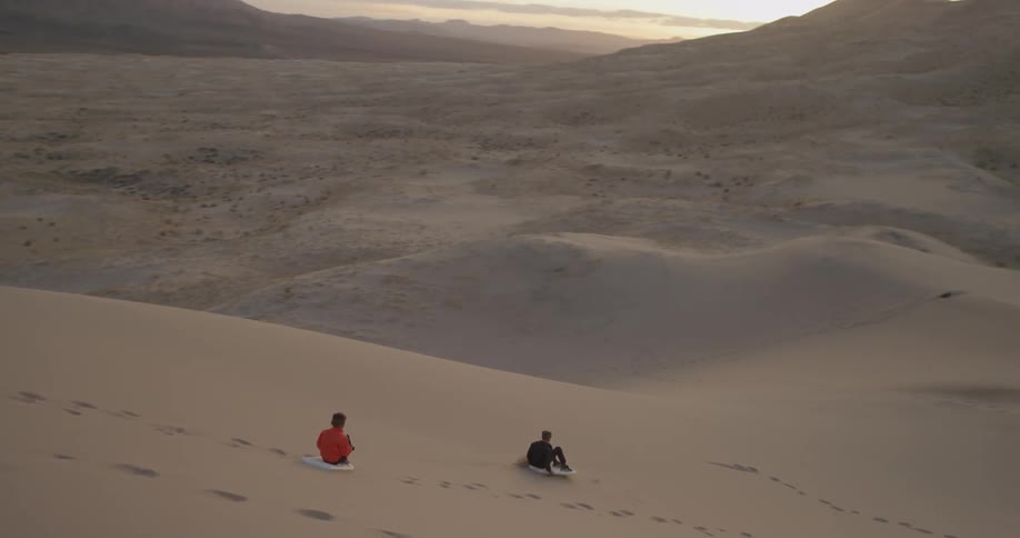 Two boys ride wakeboards down a sand dune
