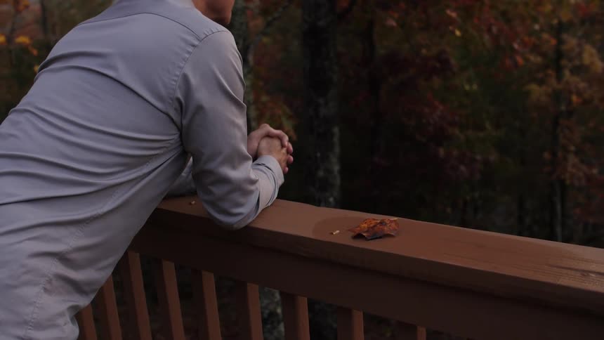 A man is leaning over his balcony looking into the woods