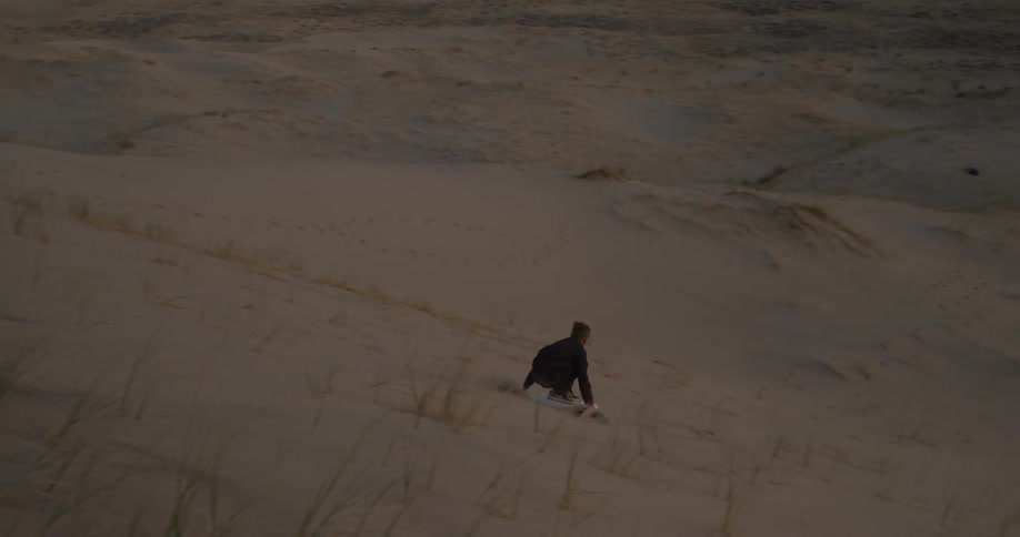 A boy rides a surfboard down a sand dune