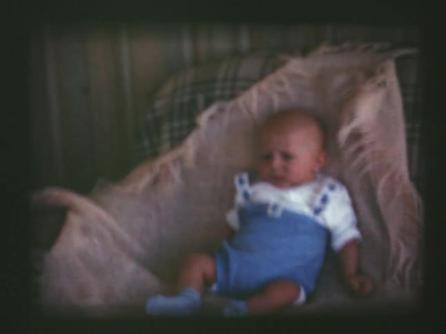 A baby lays on a blanket draped over a couch