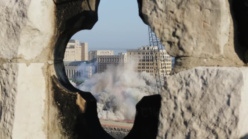 A city building is demolished and collapses to the ground in a puff of smoke
