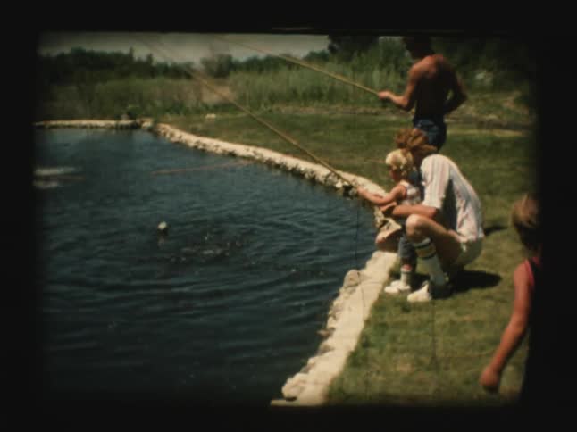 A young boy reels in a fish he caught in a pond