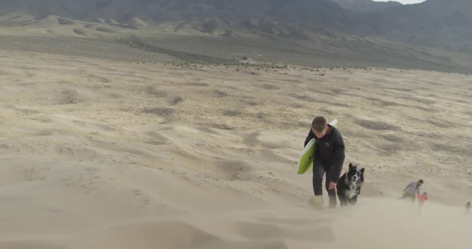 A young boy climbs a sand dune with a dog and a boogie board