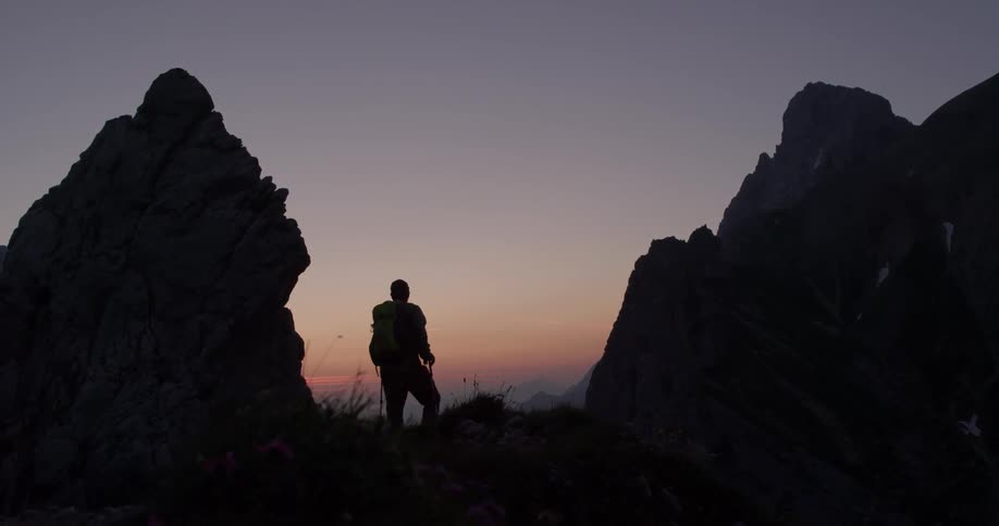 A hiker walks to the peak and stops to look at the sunset