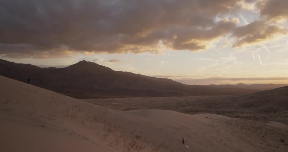 A boy is hauling a wakeboard up the side of a sand dune