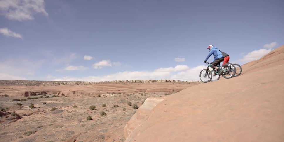 Two bicyclists perch atop a dune above a canyon