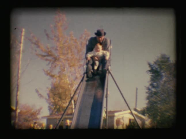 A man holds a baby and goes down the slide
