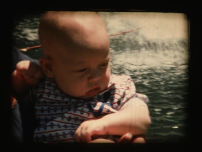 An older film of a woman holding a baby by some water