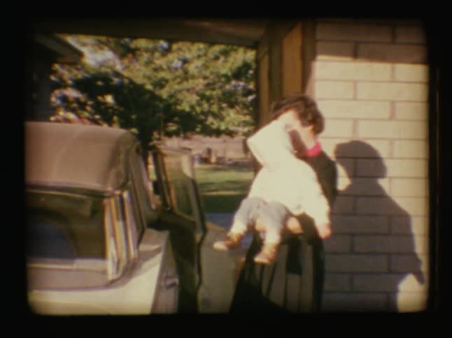 A woman carries an infant towards a car