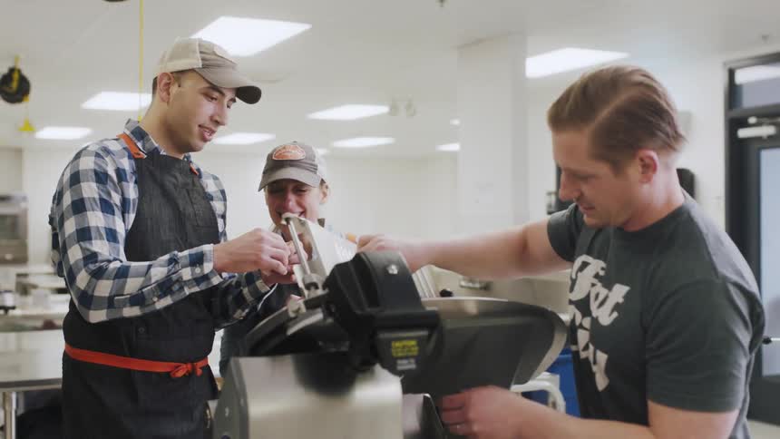 A man hands another man a piece of meat to sample