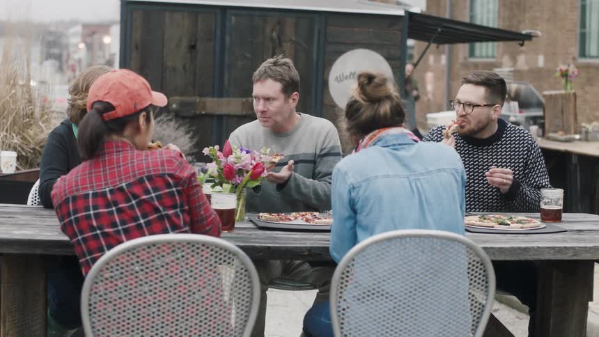 A group of people dine on pizza at an outdoor table