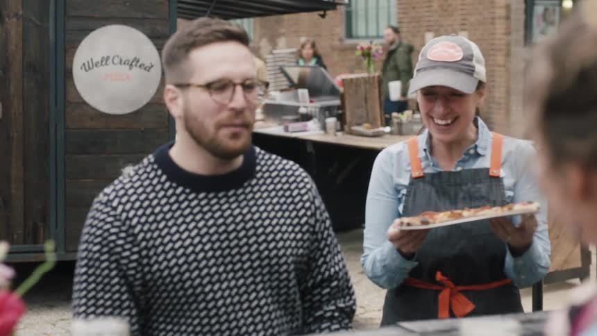 A woman serves a pizza to customers at an outdoor table