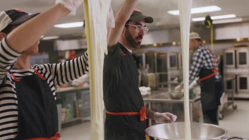 A man and a woman are working with steaming dough in a large kitchen