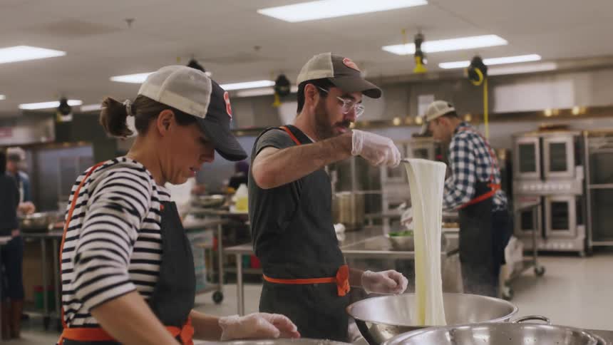 People work in a kitchen making cheese