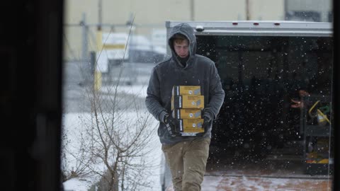 A man carries packages from a truck as it snows