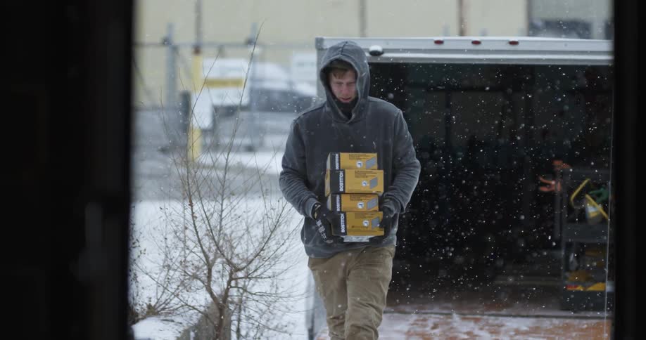 A man carries packages from a truck as it snows